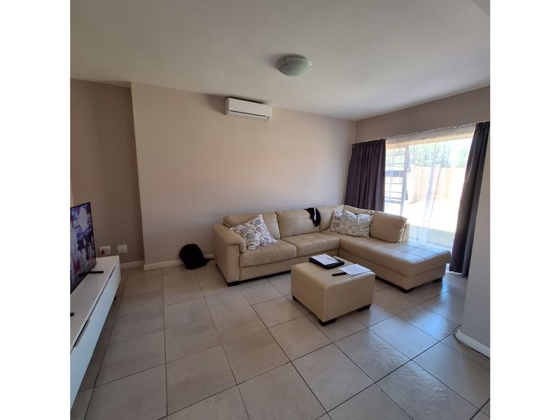 A bright living room featuring neutral tiled flooring, a wall-mounted air conditioning unit, and large sliding glass doors providing access to the exterior.