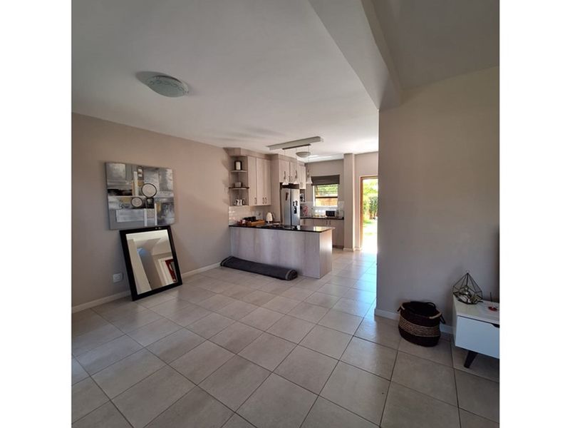 Open-plan living area featuring tiled flooring and a functional kitchen with built-in cabinetry and a breakfast counter, leading to an exterior exit.