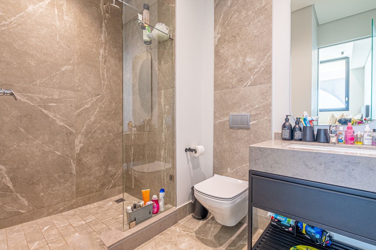 Modern bathroom featuring a walk-in shower with glass screen, wall-mounted toilet, and a sleek vanity unit with stone countertop.