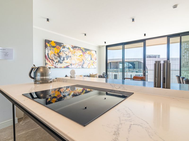 Modern open-plan kitchen area featuring a stone island with integrated induction cooktop, recessed lighting, and large sliding doors leading to a balcony.