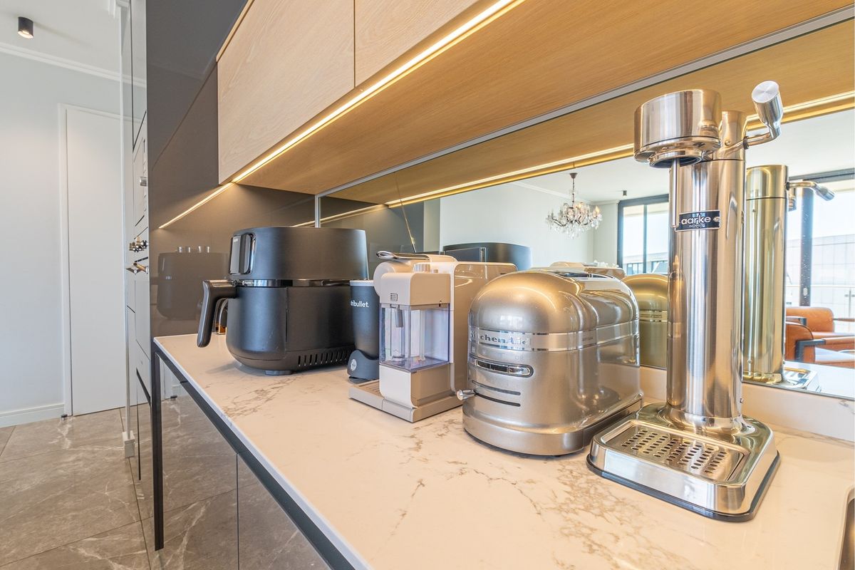 Modern kitchen area featuring a stone countertop, mirrored backsplash, and integrated under-cabinet lighting with sleek cabinetry.