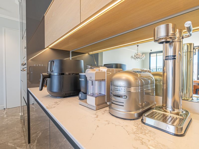 Modern kitchen area featuring a stone countertop, mirrored backsplash, and integrated under-cabinet lighting with sleek cabinetry.