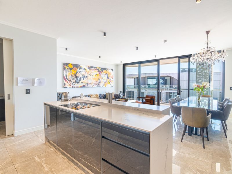 Modern open-plan living area featuring a sleek kitchen island with stone countertops, induction cooktop, and seamless flow to the dining space and balcony.
