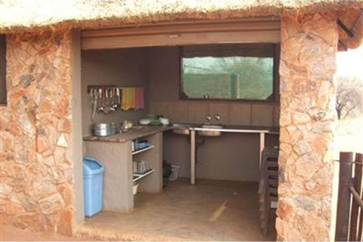 Outdoor kitchen area featuring stone masonry walls, a thatched roof overhang, and basic built-in prep counters with a stainless steel sink.