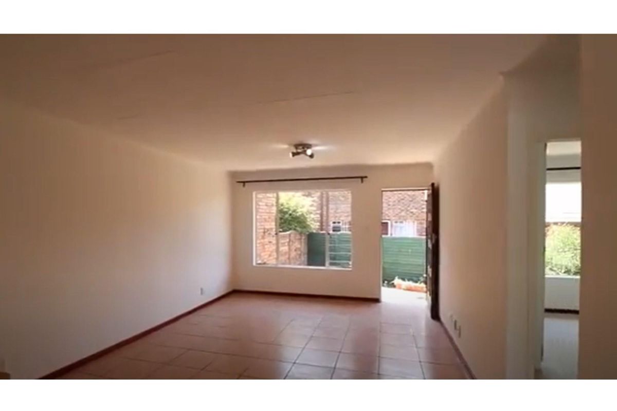 A bright, empty living area featuring tiled flooring, a large window, and direct access to an outdoor space.
