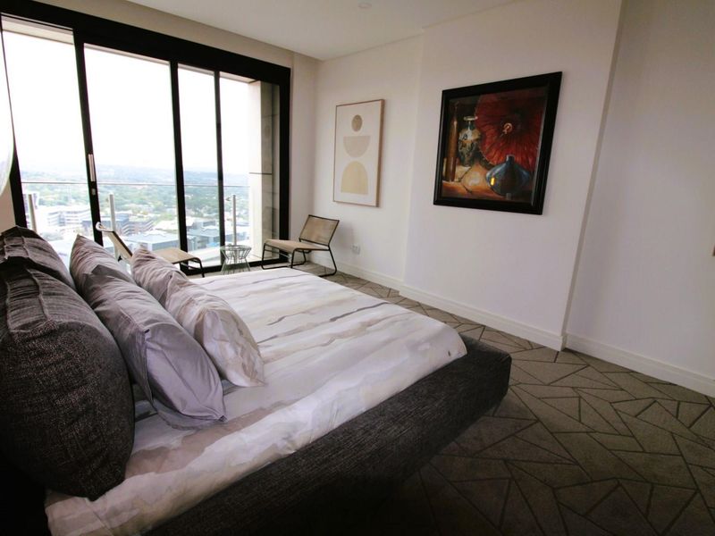A modern bedroom featuring floor-to-ceiling sliding glass doors that open onto a balcony with expansive city views.