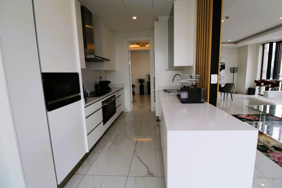 Modern galley-style kitchen featuring sleek white cabinetry, stone countertops, integrated oven, built-in microwave, and a stainless steel extractor fan with polished marble-look floor tiles.