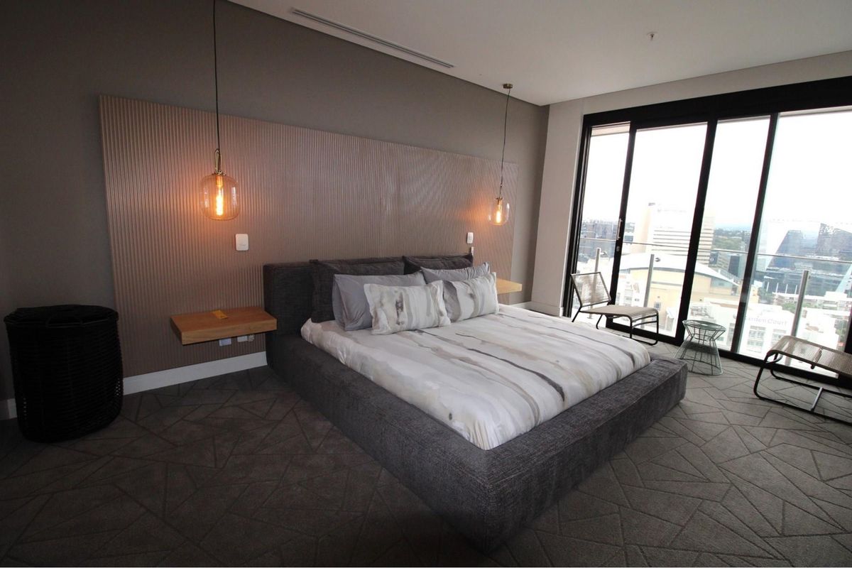 Modern bedroom featuring a textured feature wall, floating bedside shelves, pendant lighting, and large sliding glass doors leading to a balcony with city views.