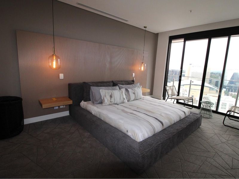 Modern bedroom featuring a textured feature wall, floating bedside shelves, pendant lighting, and large sliding glass doors leading to a balcony with city views.