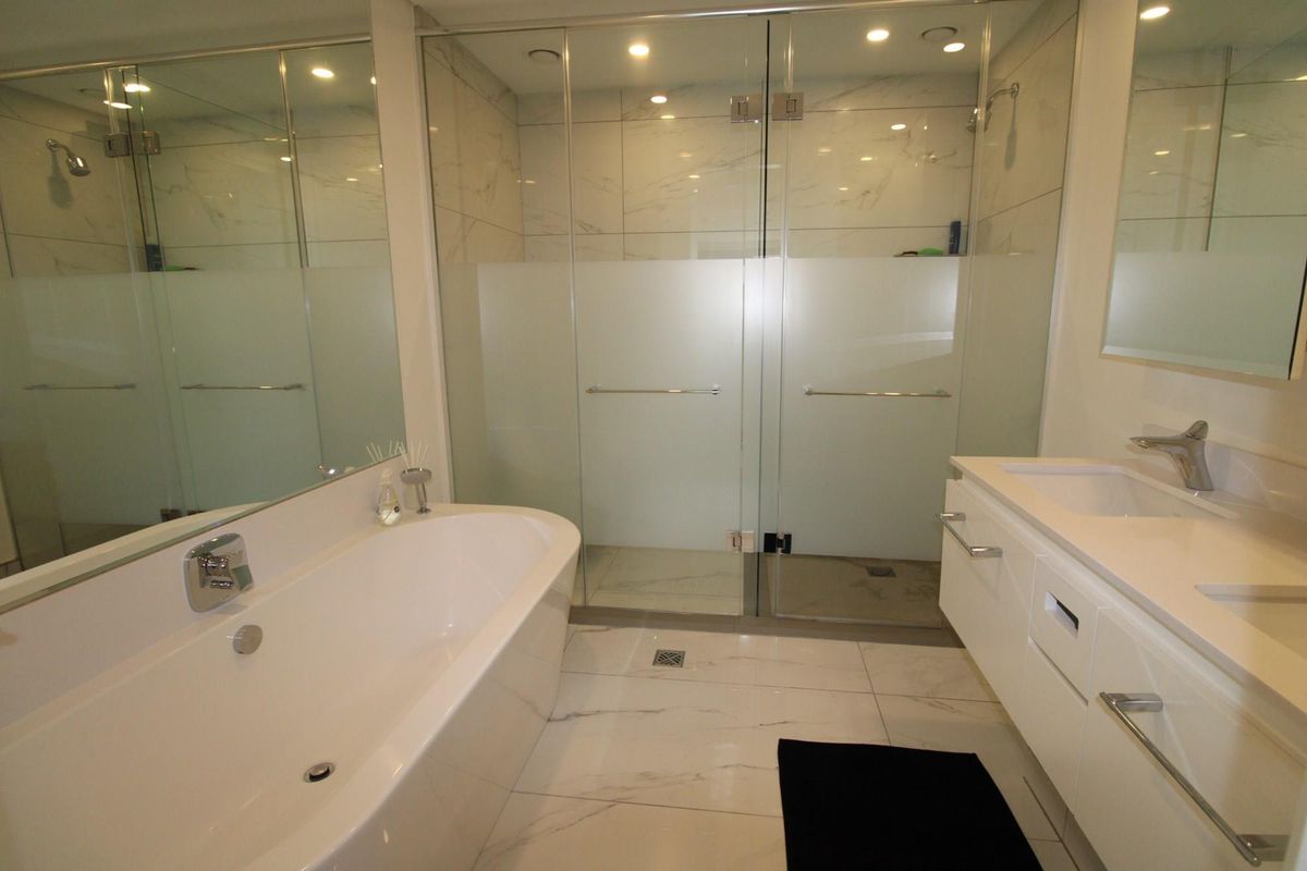 Modern bathroom featuring a freestanding bathtub, a large walk-in glass shower, and a sleek vanity with integrated sink and marble-look floor tiles.