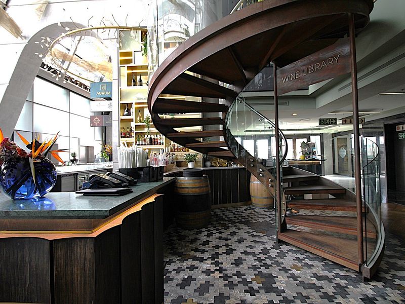Sophisticated bar area featuring a striking spiral staircase with glass balustrades, custom built-in bar counter, and intricate patterned floor tiling.