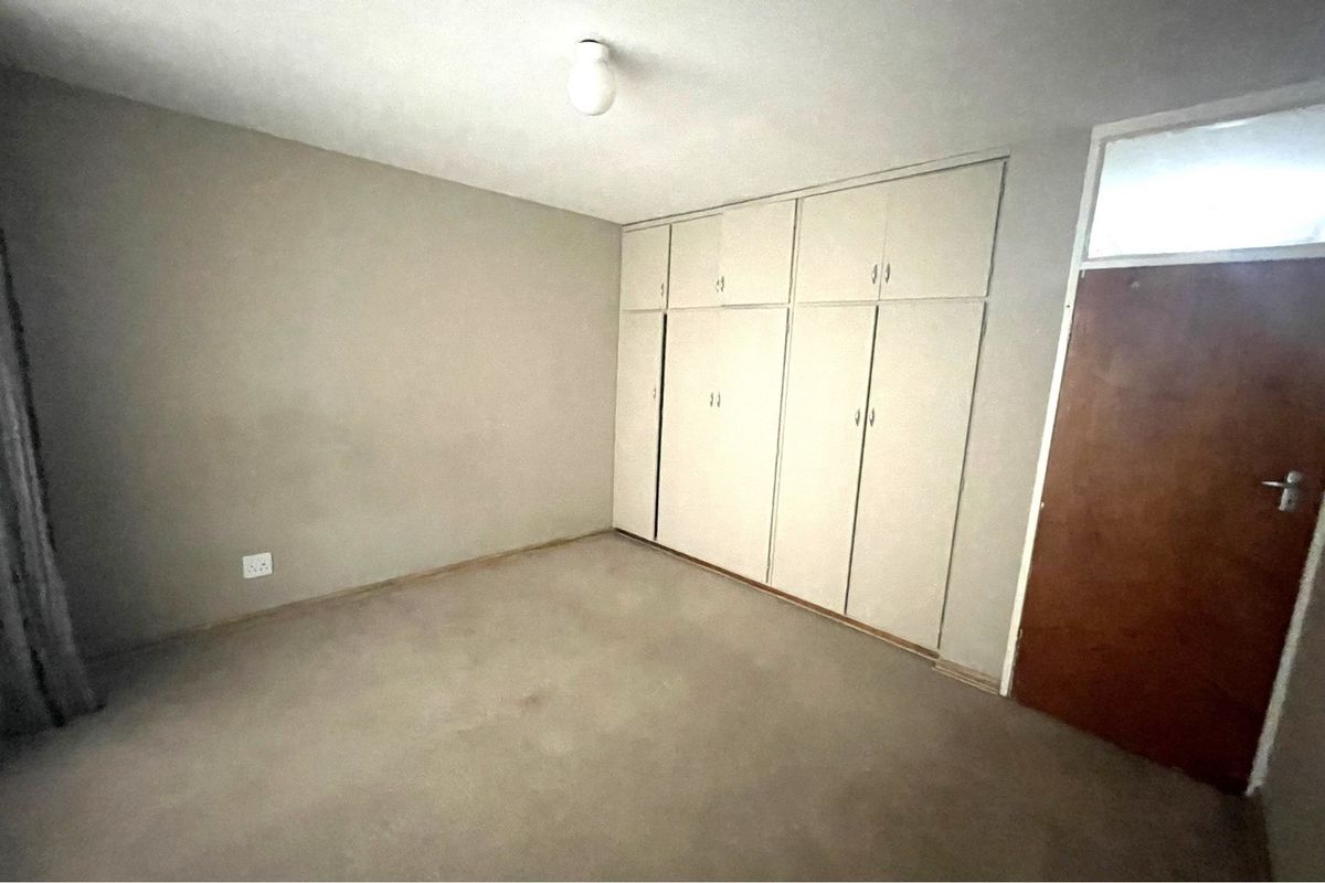 An empty bedroom featuring built-in cupboards, neutral wall finishes, and carpeted flooring, offering a blank canvas for personalization.