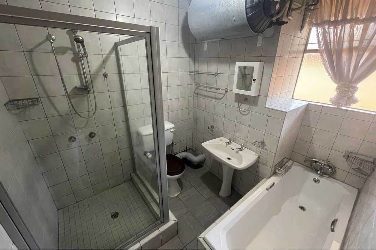 A functional bathroom featuring a separate shower enclosure, a bathtub, a pedestal basin, and a toilet, with exposed plumbing and a wall-mounted water heater.