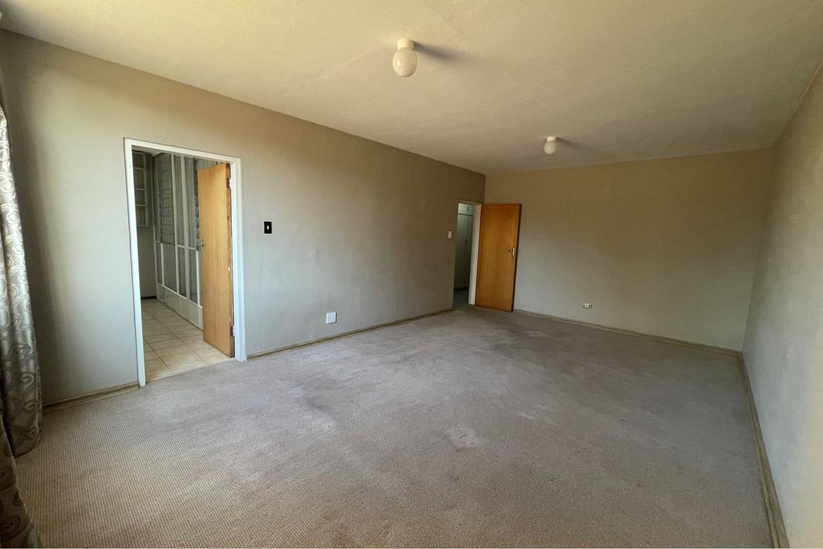 A spacious, empty living room featuring neutral wall tones, wall-to-wall carpeting, and access to adjacent rooms through standard wooden doors.