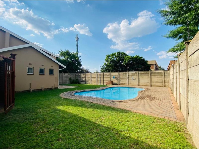 Private backyard featuring a kidney-shaped swimming pool, paved surround, and established lawn enclosed by high precast concrete boundary walls.