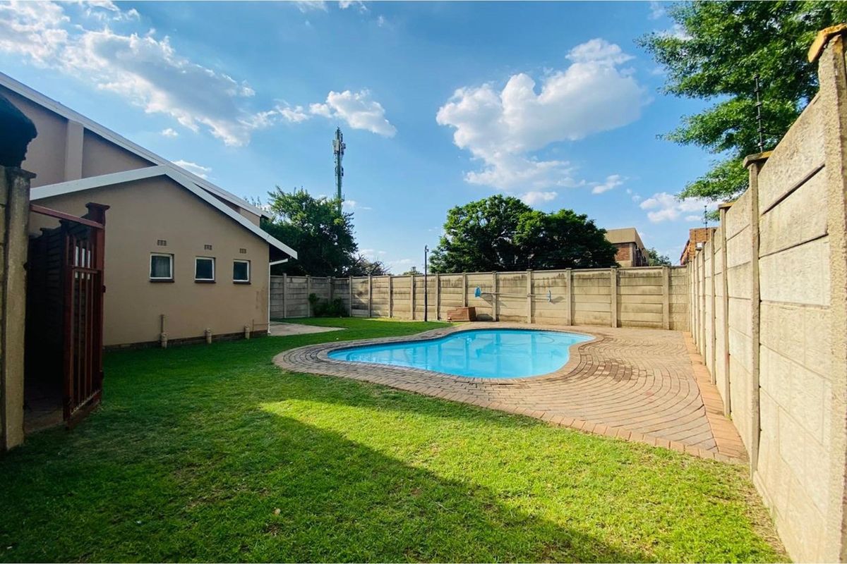 Private backyard featuring a kidney-shaped swimming pool, paved surround, and established lawn enclosed by high precast concrete boundary walls.