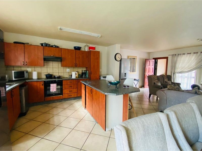 Open-plan kitchen and living area featuring wooden cabinetry, a central island, and tiled flooring throughout the space.