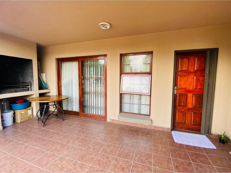 Covered patio area featuring a built-in braai, tiled flooring, and direct access to the interior through sliding glass doors and a solid timber door.