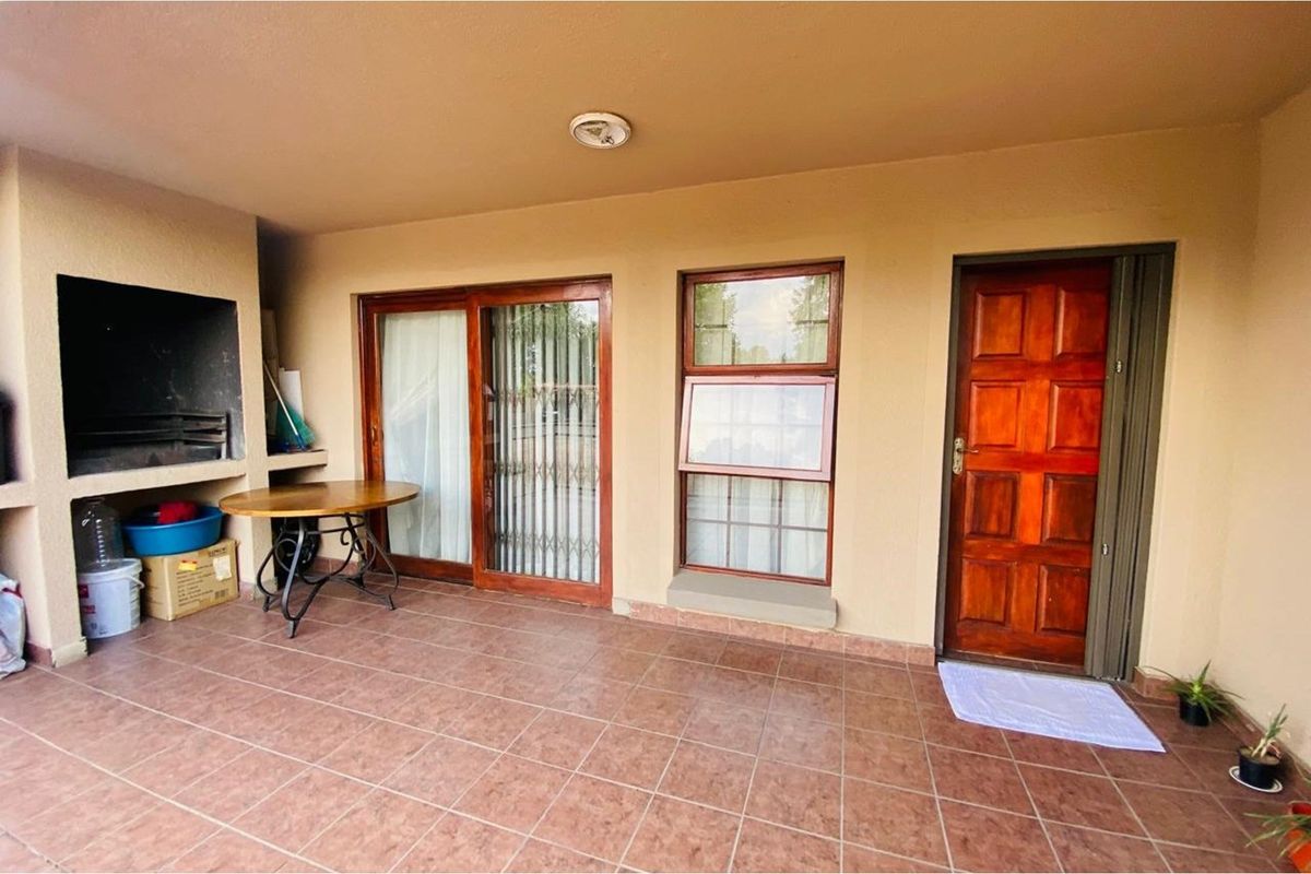 Covered patio area featuring a built-in braai, tiled flooring, and direct access to the interior through sliding glass doors and a solid timber door.