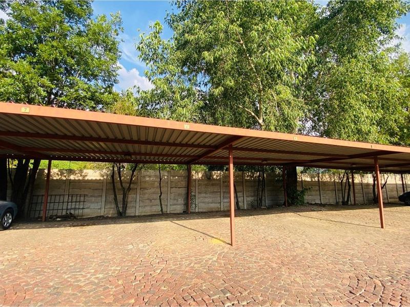 Covered carport area with paved driveway surface and perimeter boundary wall, providing sheltered parking space for vehicles.