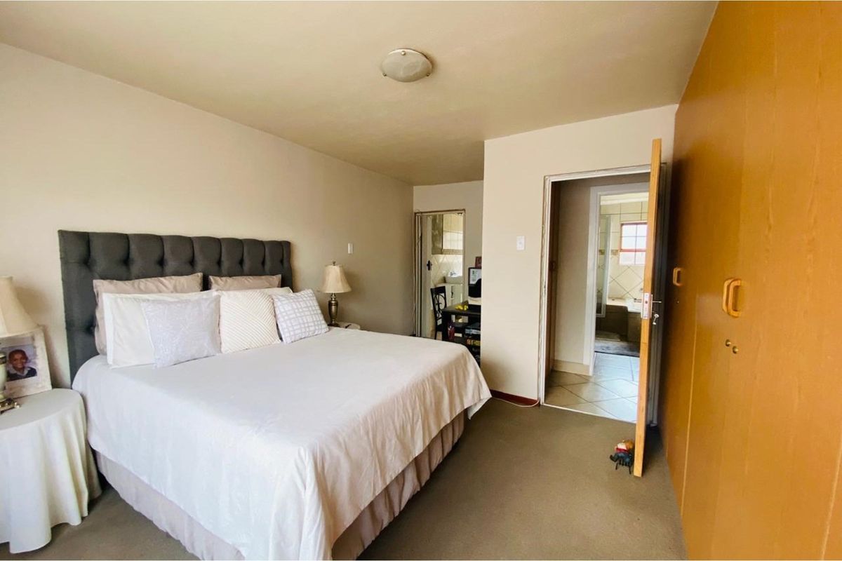 A bedroom featuring built-in wooden cupboards and an en-suite bathroom, finished with neutral carpeting and standard ceiling lighting.