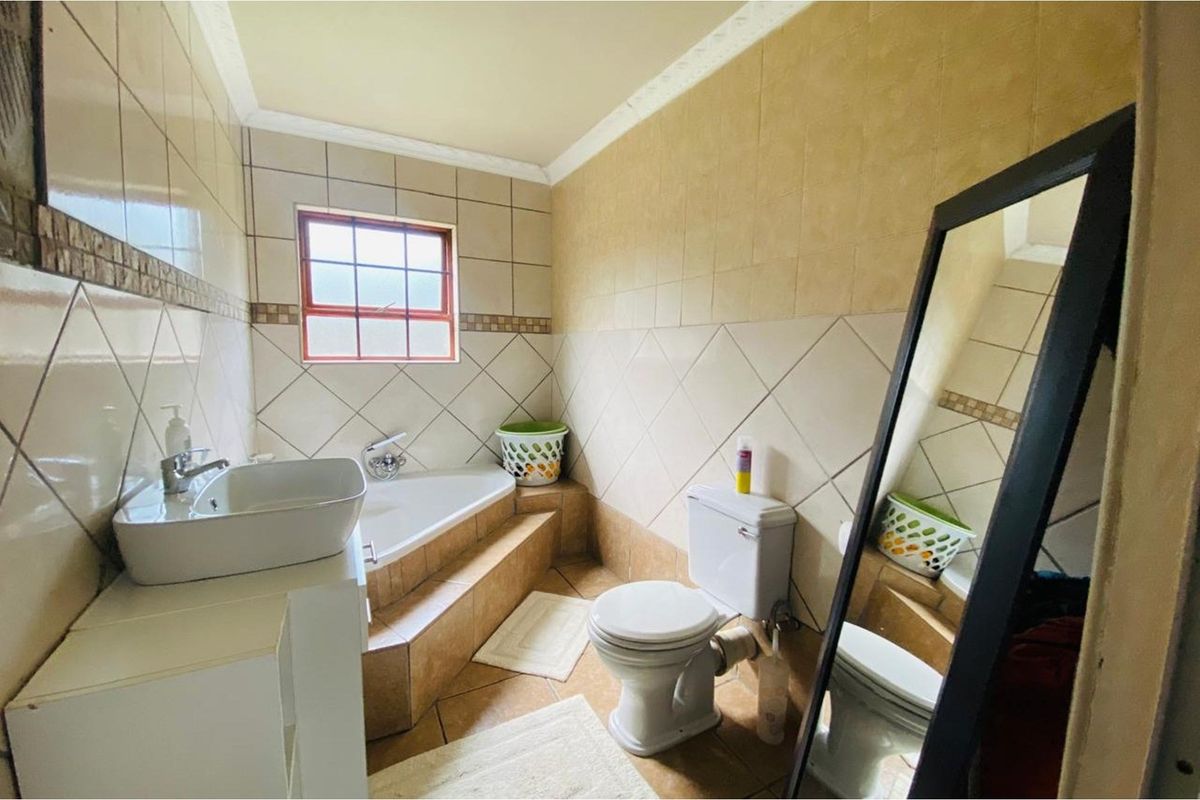 A functional bathroom featuring a built-in corner bathtub, a pedestal-style basin, and a standard toilet with tiled walls and flooring.