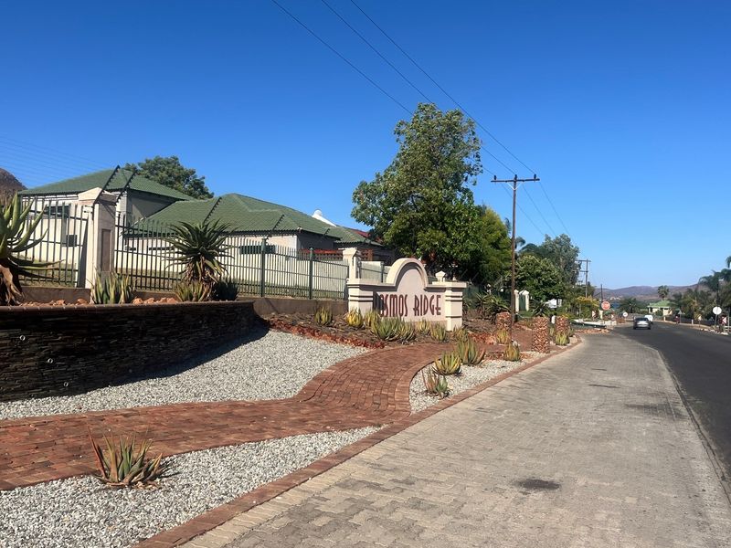 Street view of the Cosmos Ridge estate entrance, featuring a paved walkway, landscaped garden beds with aloes, and a stone-clad retaining wall.