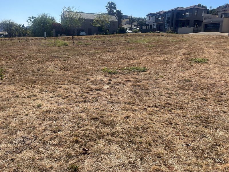 A vacant residential plot of land featuring dry grass, situated in an established neighborhood with surrounding residential properties.