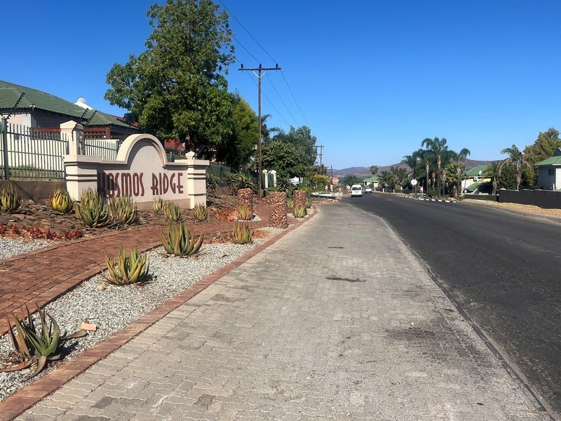 Street view of the Cosmos Ridge estate entrance, featuring paved sidewalks, landscaped garden beds with aloes, and established perimeter fencing.