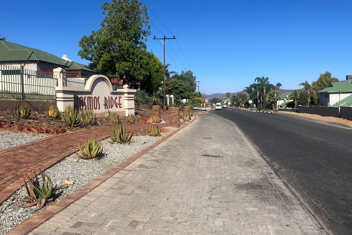 Street view of the Cosmos Ridge estate entrance, featuring paved sidewalks, landscaped garden beds with aloes, and established perimeter fencing.