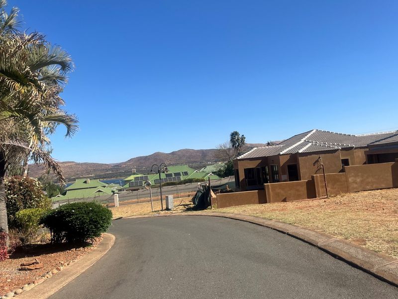 A view of a residential street featuring paved roads, landscaped garden areas, and surrounding properties with mountain views in the background.
