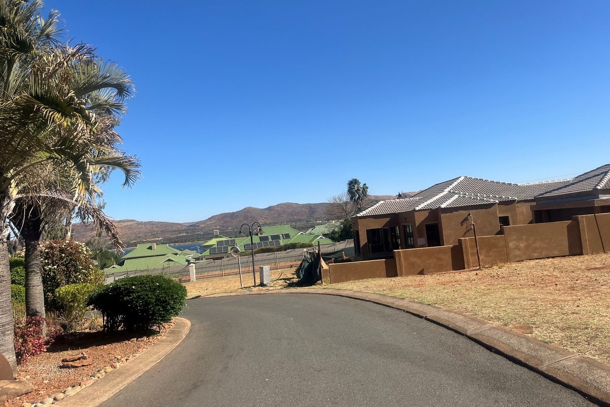 A view of a residential street featuring paved roads, landscaped garden areas, and surrounding properties with mountain views in the background.