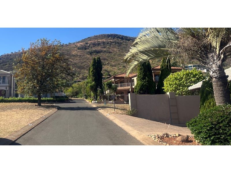 A view of the residential street approach within the estate, featuring paved roads, established landscaping, and surrounding hillside views.