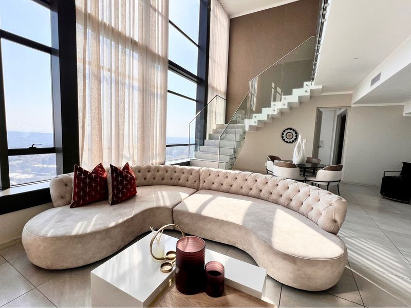 Spacious double-volume living area featuring floor-to-ceiling windows with panoramic views and a modern floating staircase with glass balustrades.