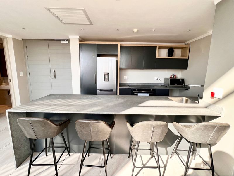 Modern kitchen featuring a large central island, sleek dark cabinetry, integrated appliances, and high-quality tiled flooring in a contemporary penthouse setting.