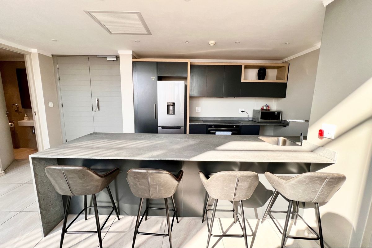 Modern kitchen featuring a large central island, sleek dark cabinetry, integrated appliances, and high-quality tiled flooring in a contemporary penthouse setting.