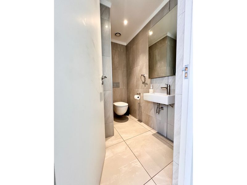 A modern, minimalist guest bathroom featuring neutral large-format floor and wall tiles, a wall-mounted basin, and a concealed cistern toilet.