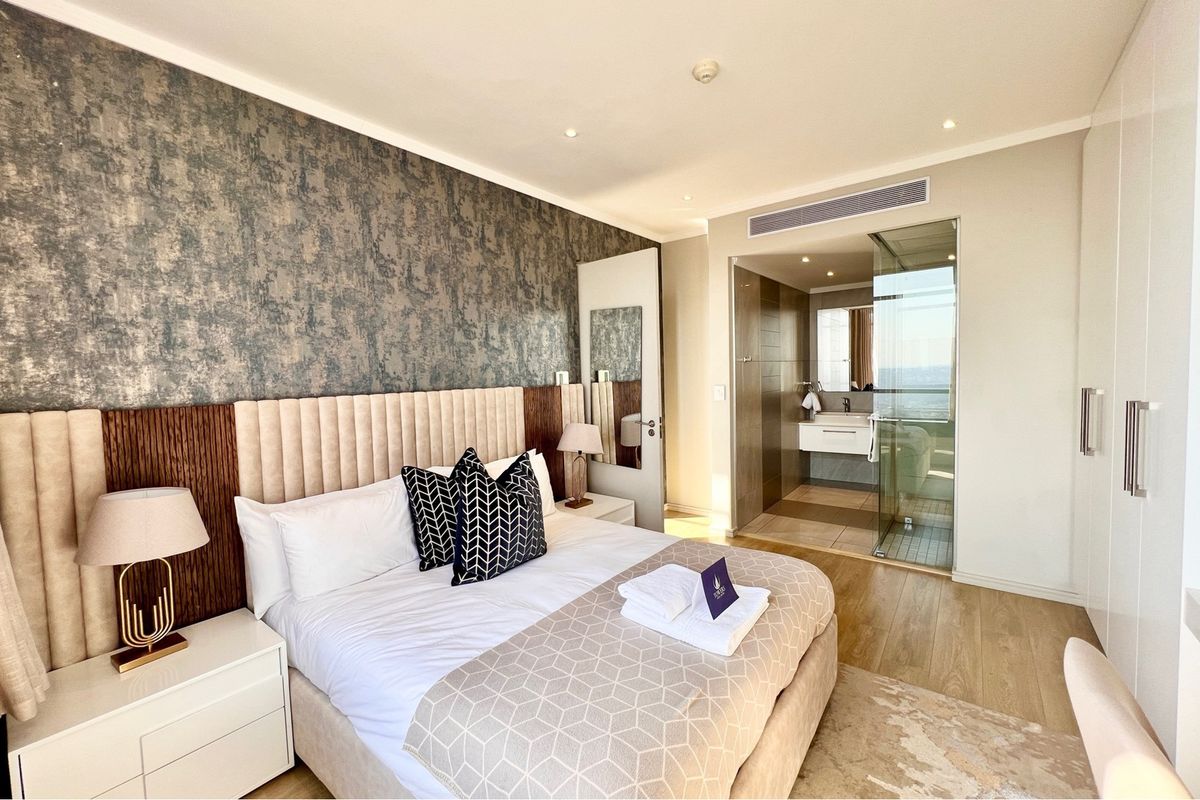 Modern bedroom featuring a textured feature wall, integrated lighting, and an en-suite bathroom with a glass-enclosed shower and contemporary vanity.