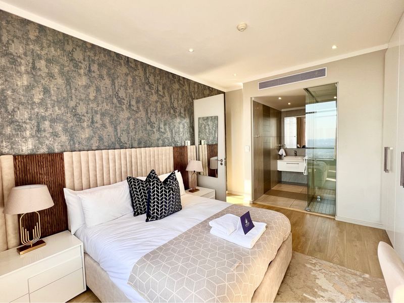 Modern bedroom featuring a textured feature wall, integrated lighting, and an en-suite bathroom with a glass-enclosed shower and contemporary vanity.
