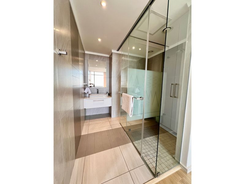 Modern bathroom featuring a spacious walk-in glass shower, wall-mounted vanity with basin, and neutral floor-to-ceiling tiling.