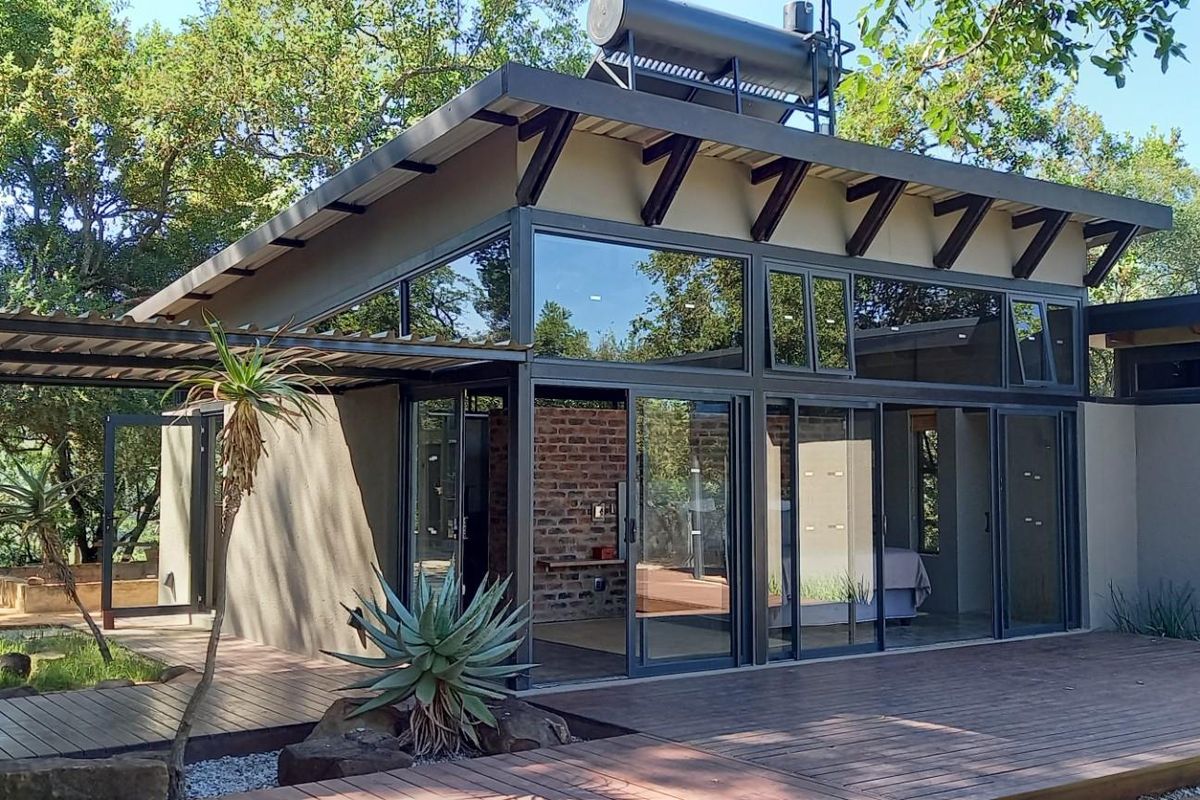 Modern architectural home featuring expansive glass sliding doors, a timber deck, and a solar water heating system set within a natural wooded environment.