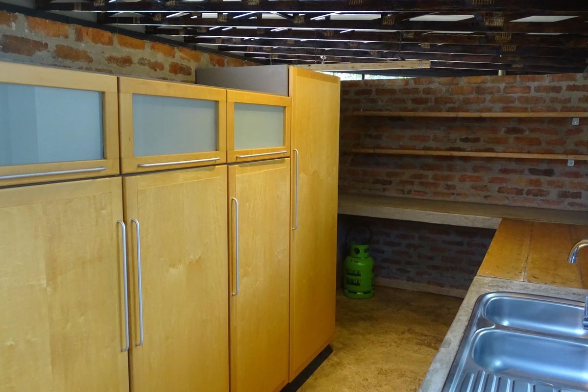 A rustic kitchen area featuring wooden cabinetry, a double stainless steel sink, and exposed brick walls with open shelving.