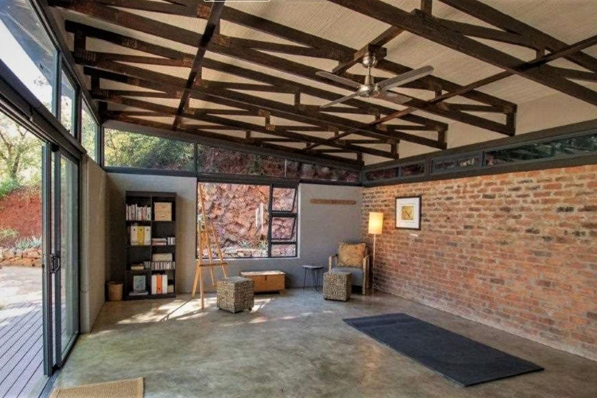Spacious living area featuring exposed timber roof trusses, polished concrete flooring, and a prominent feature brick wall with large sliding glass doors.