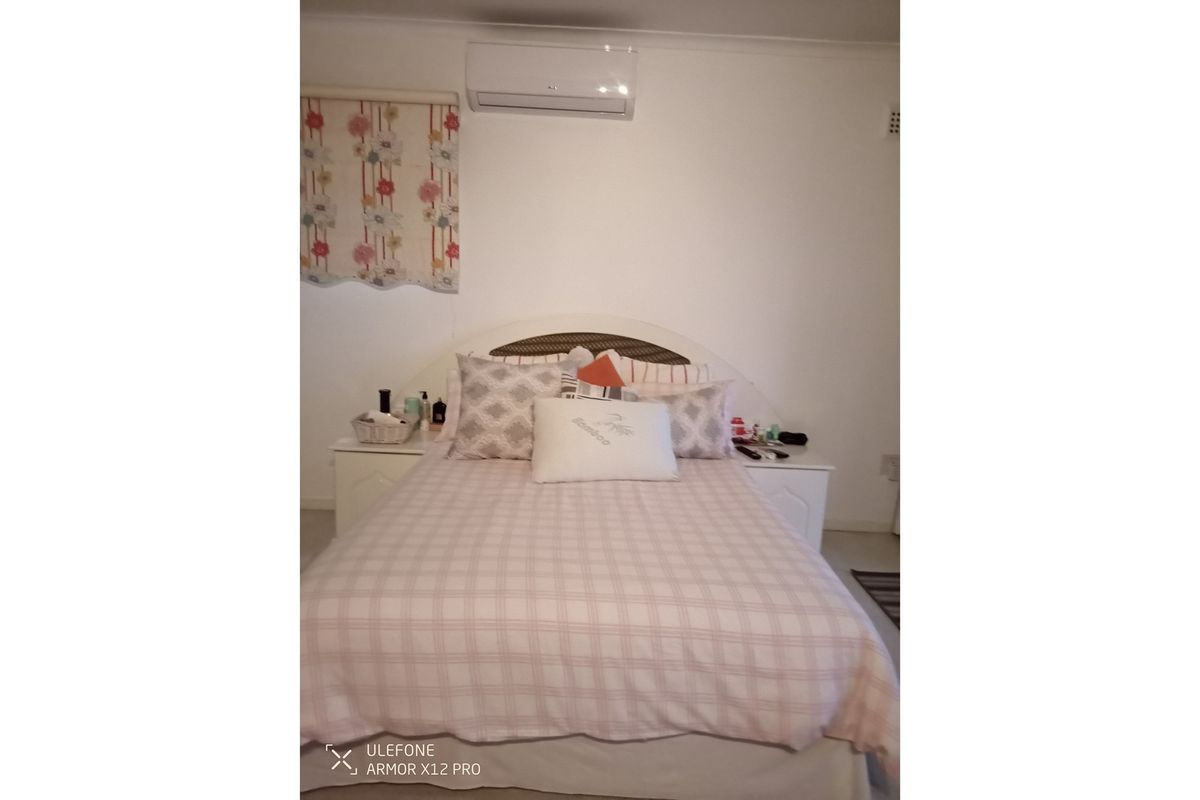 A bedroom featuring a wall-mounted air conditioning unit and a roller blind.
