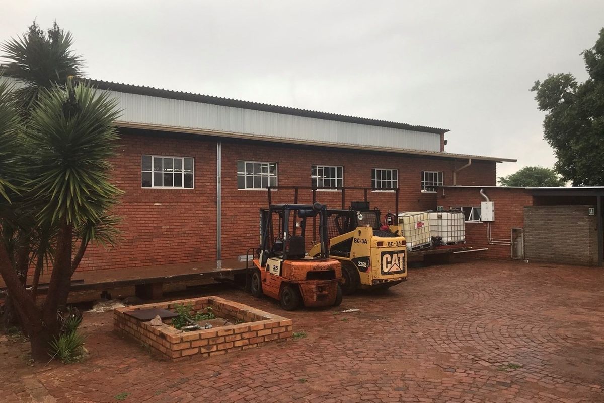 Exterior view of a brick farm building featuring a loading platform, metal roof, and paved yard area.