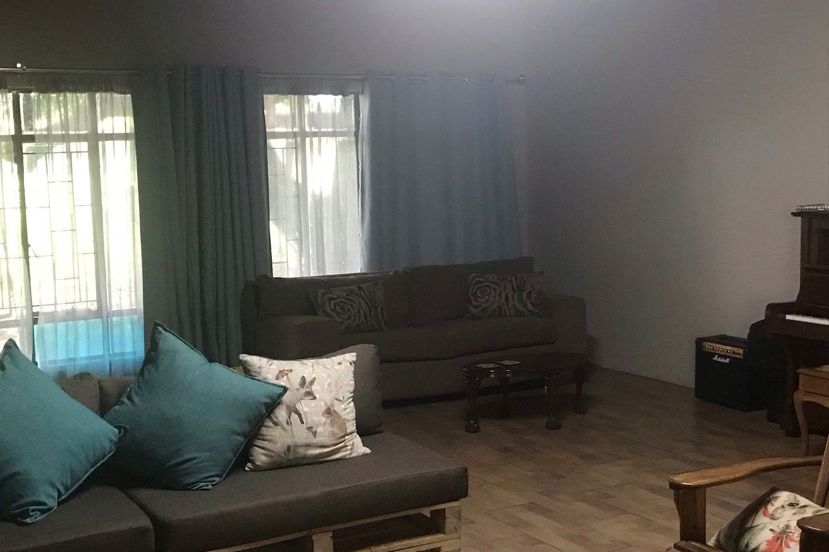A living room featuring tiled flooring and large windows with curtains, providing natural light and a view of the exterior.