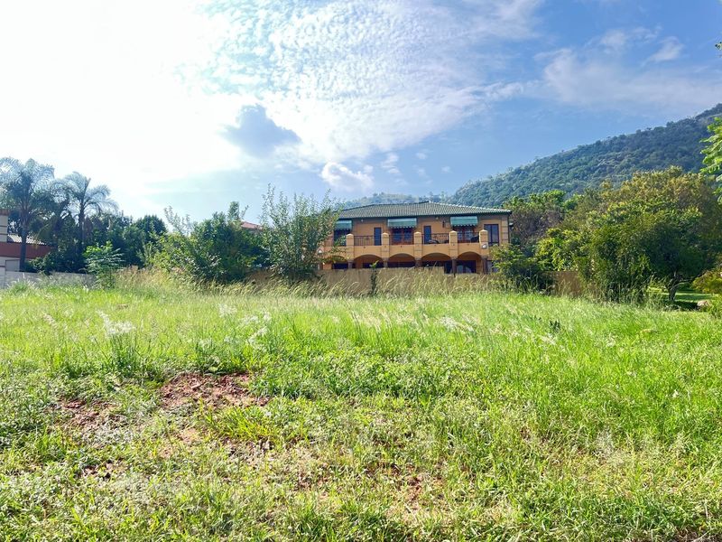 A view of a vacant residential plot featuring natural grass coverage with established trees and neighbouring properties in the background.