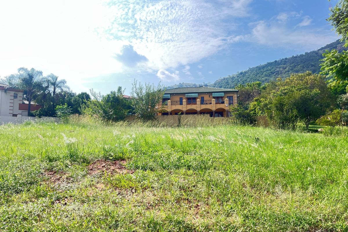 A view of a vacant residential plot featuring natural grass coverage with established trees and neighbouring properties in the background.