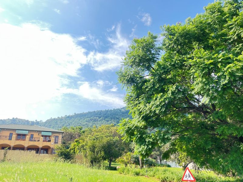 A scenic view of a residential property featuring lush greenery, mature trees, and a mountain backdrop, showcasing the peaceful surroundings of the vacant land.
