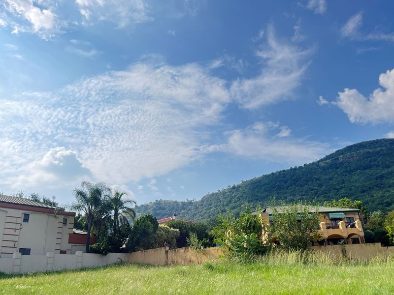 A view of a vacant residential plot featuring surrounding established homes and a scenic mountain backdrop.